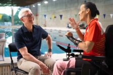 Apple CEO Tim Cook sat on a chair with a swimming pool in the background talking to Professional Paralympic Swimmer; Teresa Perales uses the Apple Watch for her insane training.